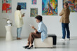 © pressmaster - Woman resting on couch and using smartphone during her visit to art gallery