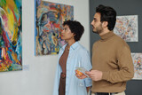Fototapeta Na drzwi - Multiethnic couple watching paintings on the wall while visiting art gallery
