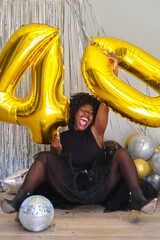 African woman in a 40 birthday party with 40 birthday golden balloons on the floor.