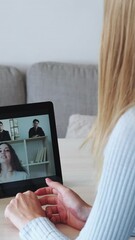 Wall Mural - Vertical video. Internet conference. Virtual office. Online brainstorm. Woman listening to business colleagues on distance teamwork call on tablet in light interior at home.