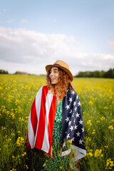 Wall Mural - Young woman with american flag on blooming meadow. 4th of July. Independence Day. Patriotic holiday. USA flag fluttering in the wind.