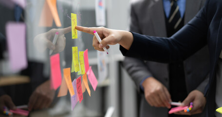 Businessperson teamwork meeting in office and use sticky post notes to brainstorming ideas on glass board. Asian businesswoman planning corporate strategy with colleague for success startup business.