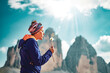 © Michael - Young woman blows seed from a dandelion in the afternoon. Tre Cime, Dolomites, South Tirol, Italy, Europe.