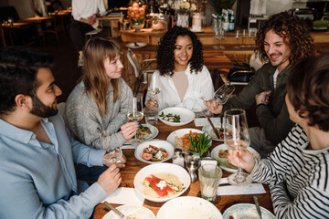 Wall Mural - Group of cheerful friends talking and drinking wine while dining in restaurant