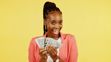 Finance, Fan And Winner With A Black Woman In Studio On A Yellow Background Holding Cash, Money Or Wealth. Financial, Investment And Trading With Dollar Bills In The Hand Of A Female After Winning