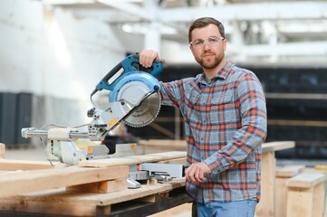 Wall Mural - Wood cutting table with electric circular saw. Professional carpenter in uniform cutting wooden board at sawmill carpentry manufacturing . Sawing machine