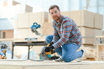 Wall Mural - A carpenter works on woodworking the machine tool. Man collects furniture boxes. Saws furniture details with a circular saw. Process of sawing parts in parts. Against the background of the workshop.