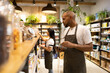 © ADDICTIVE STOCK - Ethnic salesman in apron standing near shelf in grocery store