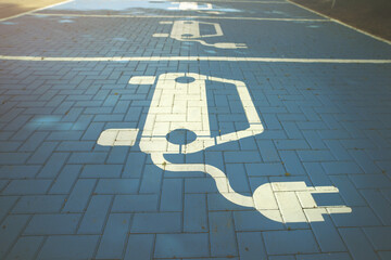 white electric car symbol painted on blue pavement. parking lot with charging station marked for battery electric vehicles. selective focus. modern mobility concept. toned colours