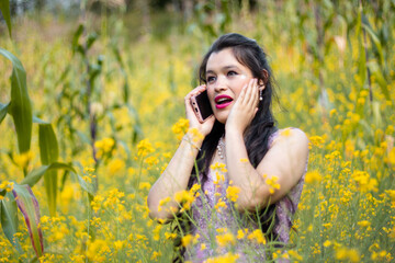 Foto de una mujer agradable hablando por celular mientras camina en un campo de flores amarillo,fondo naturaleza,bosque,mujer bonita con telefono