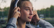 Closeup Portrait of Beautiful White Woman Smiling While Putting on her Headphones in the Park During her Early Morning Walk. Female Teenager Enjoying Music and Fresh Air While Being Outdoors 