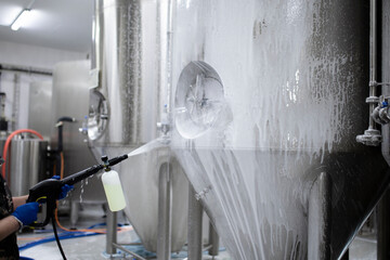 worker's hand hold a high pressure cleaner gun and put foam on equipment on the factory