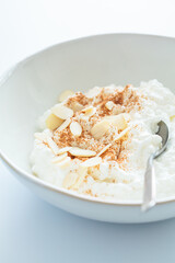 Wall Mural - Cottage cheese with cinnamon and almonds in white bowl, white background. Healthy protein breakfast concept.