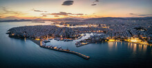 Aerial View Of The Illuminated Piraeus District In Athens, Greece, With Zea Marina, Kastella Hill And The Ferry Boat Harbour In The Background During Dusk