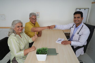 Attractive young Indian doctor sitting with a senior patient. Wide shot of a living room where a geriatric doctor is doing a domestic consultation to an elderly man and woman. 