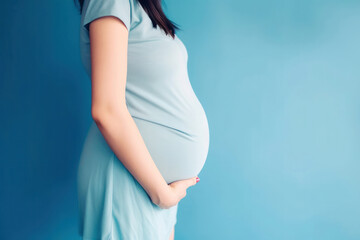 A pregnant caucasian woman in blue dress strokes her belly on blue background. Place for text. Copy space. Waiting for the birth of a child. High quality photo