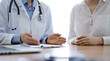 © rogerphoto - Doctor and patient discussing something while sitting near each other at the wooden desk in clinic, close up of hands. Medicine concept.