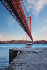 Wall Mural - View from under of 25 de Abril Bridge famous tourist landmark over Tagus river, Christ the King monument and quay. Lisbon, Portugal