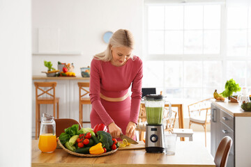 Sporty mature woman cutting lemon for healthy smoothie in kitchen