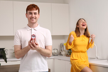 Poster - Young man with engagement ring and his happy girlfriend in kitchen