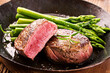 Traditional roasted angus beef steak with with green asparagus served as close-up in a rustic fying pan