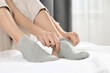 © New Africa - Woman putting on grey socks in bedroom, closeup