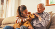 © Kitreel - Portrait of a Senior Man and his Daughter Petting the Family Dog Laying on their Lap. They are Chatting While Sitting on a Sofa. Moments of Happiness and Affection During Weekend Visit