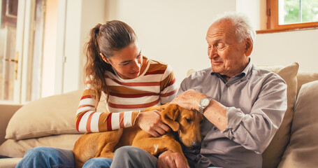 Portrait of a Senior Man and his Daughter Petting the Family Dog Laying on their Lap. They are Chatting While Sitting on a Sofa. Moments of Happiness and Affection During Weekend Visit