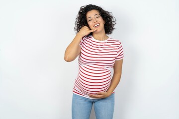 Wall Mural - young pregnant woman wearing striped t-shirt over white background smiling doing phone gesture with hand and fingers like talking on the telephone. Communicating concepts.