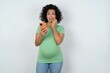 Afraid funny young pregnant woman wearing green t-shirt over white background holding telephone and bitting nails