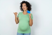 Young Pregnant Woman Wearing Green T-shirt Over White Background Hold Credit Card Point Empty Space