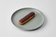 French eclair with chocolate glaze in a plate on a gray background