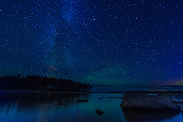 Wall Mural - night landscape with a starry sky over sea water with stones and forest. astrophotography with many 