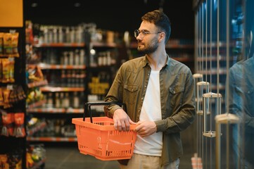 Portrait of smiling handsome man grocery shopping in supermarket, choosing food products from shelf