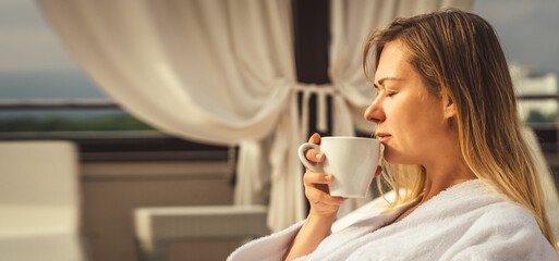 Wall Mural - Woman in white bathrobe lying on sofa and relaxing with orange cocktail at the roof.