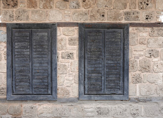 Vintage ancient wall from old sandy limestone and two closed windows with wooden shutters front view close-up