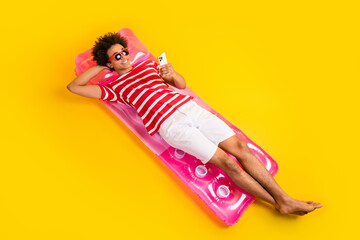 Canvas Print - Full length photo of cute pretty man wear striped t-shirt tanning inflatable mattress chatting gadget isolated yellow color background