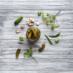 Wall Mural - Open jar with pickled cucumbers and cucumber on a fork on a wooden background, top view, copy space.