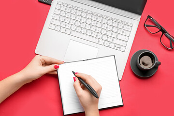Female hands with notebook, pen, cup of coffee, eyeglasses and laptop on red background