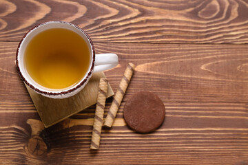 Wall Mural - Drink coaster with cup of tea, wafer rolls and cookie on wooden table