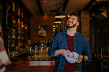 Waiter standing at a bar counter and looking at the shiny glass in a restaurant or a pub.