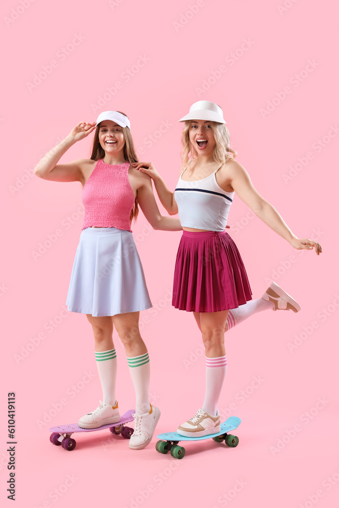 Young sisters with skateboards on pink background