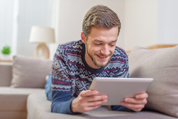Young positive man with tablet computer in their hands, on the couch at home.