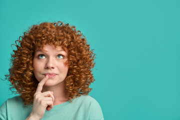 headshot portrait of thoughtful pensive young ginger woman with curly hair holding finger on lips lo