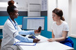 © DC Studio - African american doctor prescribing pill bottle medication to patient. Healthcare specialist during medical checkup in clean modern hospital office offering diagnosis to woman.
