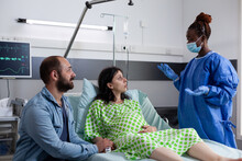 African american surgeon wearing protective gloves and mask discussing with pregnant woman explaining birth surgery in hospital ward. Woman with pregnancy lying in bed having contractions