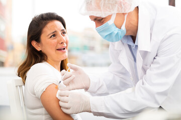 Doctor male giving Covid-19 or flu antivirus vaccine shot to female patient at health clinic or hospital office