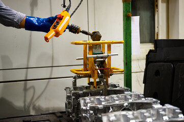 Wall Mural - Warehouse of an automobile plant, a worker lifts the cylinder block of an internal combustion engine with a special grip