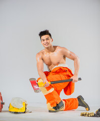 Wall Mural - With a confident smile on his face, the topless professional firefighter sits and kneels down gripping an iron axe firmly in both hands.