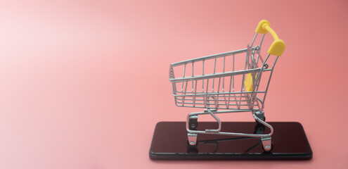 Online shopping on smart phone for global concept. shopping cart with a smartphone on pink background. buy in the online shop by mobile app. Easy shopping with fingertips for consumers. eCommerce.